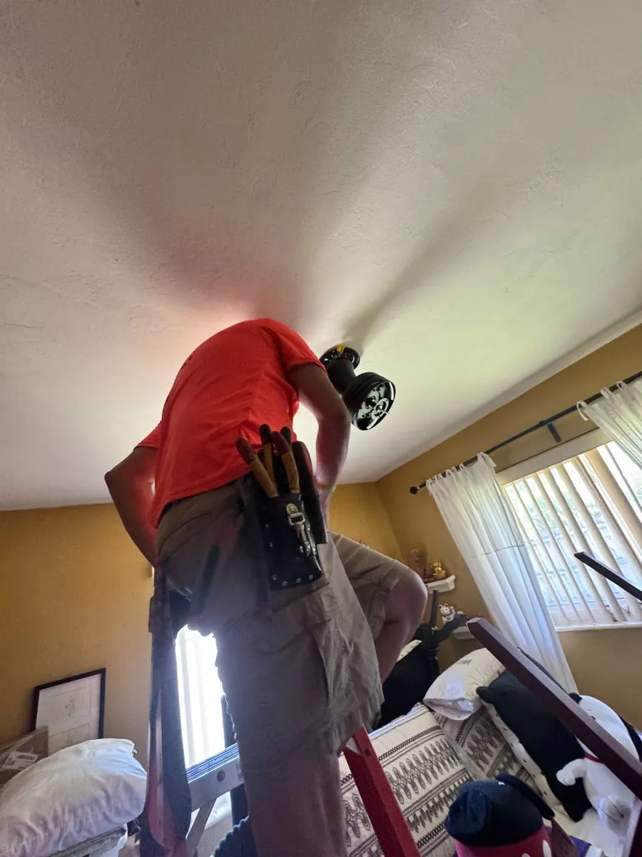 Electrician on a ladder installing a bedroom ceiling fan