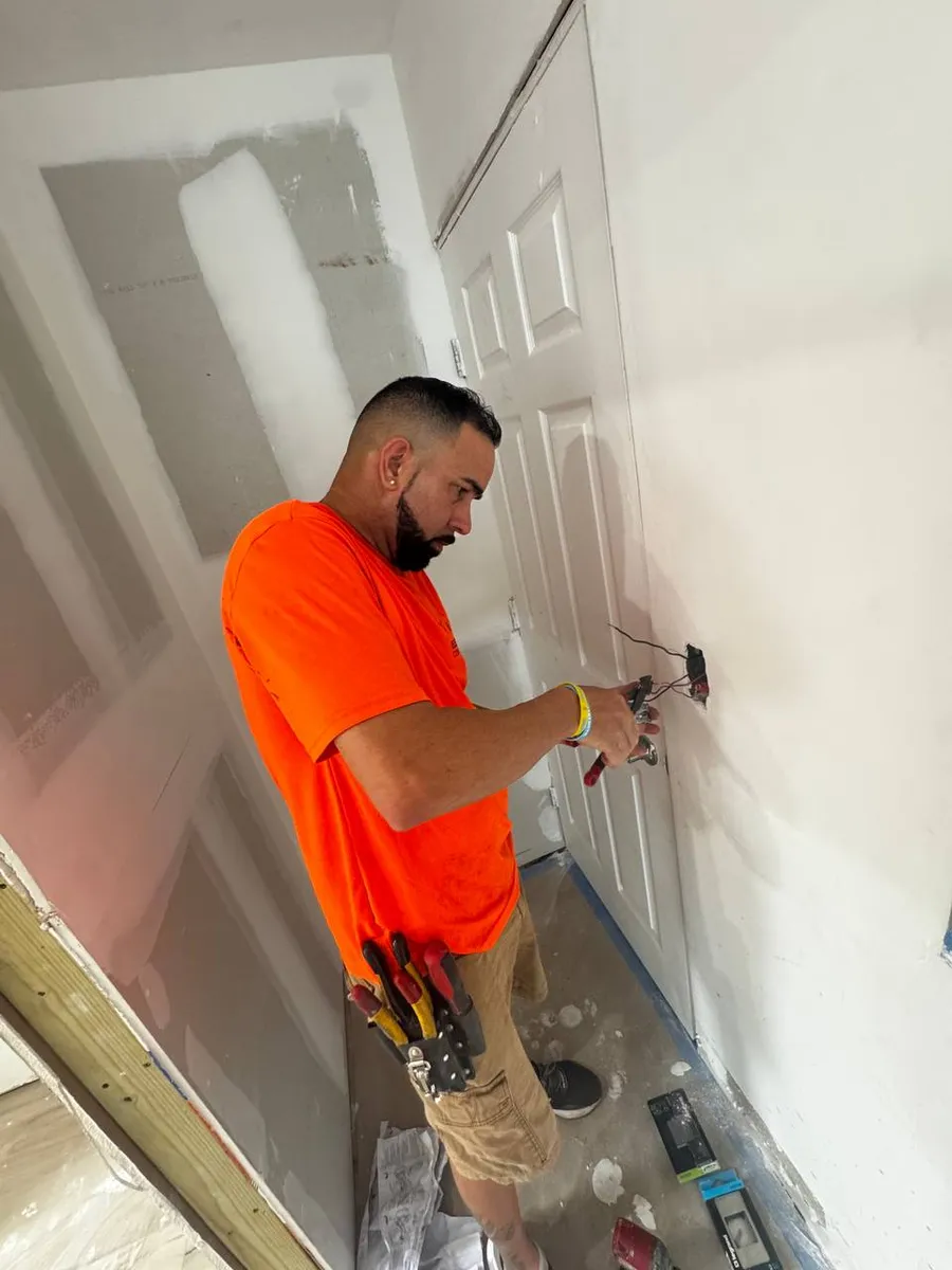 Electrician wiring a new outlet in a freshly drywalled hallway