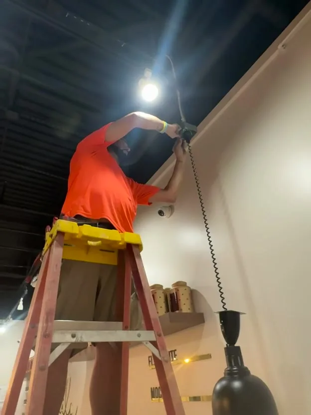 Y&M electrician on a ladder wiring a pendant light in a coffee shop